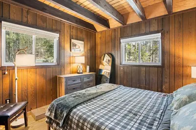 a bedroom with wooden walls and a bed and two windows at Crooked Ear Cabin in Wilmington