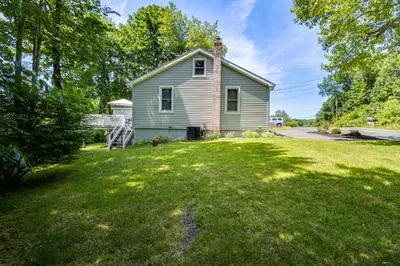 a small house in a yard with a grassy field at Modern Terryville Cottage with Deck and Lake View! in Terryville