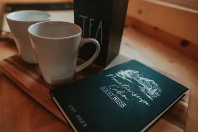 a book sitting next to two cups on a table at Mountainscape: Peaceful & Skiing in Roxbury