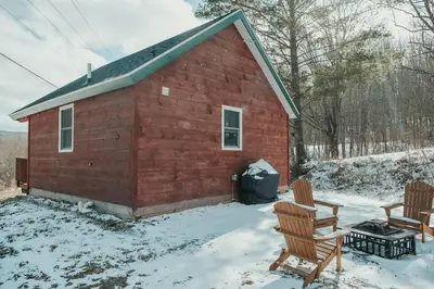 a red barn with two chairs and a table in the snow at Mountainscape: Peaceful & Skiing in Roxbury