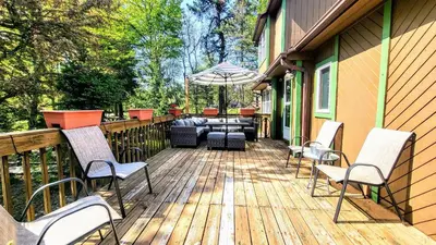 a deck with chairs and an umbrella on a house at The Wooden Nest by AvantStay Deck Big Yard w Hammocks Fire Pit in Long Pond