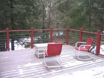 two red chairs and a table on a wooden deck at STREAMSIDE CABIN IN THE CATSKILLS in Chichester