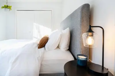 a bed with white pillows and a table with a lamp at Woodstock Retreat- Heated Pool/Hot Tub/FirePit in Saugerties