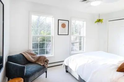 a bedroom with a bed and a chair and windows at Woodstock Retreat- Heated Pool/Hot Tub/FirePit in Saugerties
