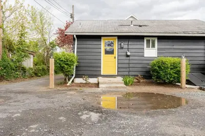 a black house with a yellow door and a driveway at Retro Retreat: 1br home w/ WFH desk, livingroom, and fire pit in Kingston