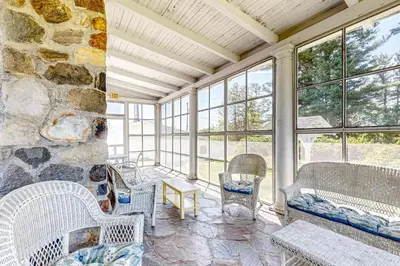 a room with chairs and a stone wall with windows at Group Getaway on Working Farm! Near Saratoga in Ballston Lake