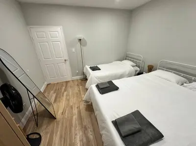 two beds in a room with white walls and wooden floors at Cozy 3 BR suite, 15 min to NYC &Times Sq in North Bergen