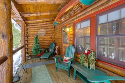 a log cabin porch with two chairs and christmas trees at Lake and Beach Access at Lake Luzerne Cabin! in Lake Luzerne