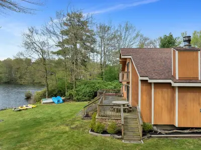 a house with a deck next to a body of water at Lakefront Family Home, Kayaks, Hot Tub, Fireplace in Lake Ariel