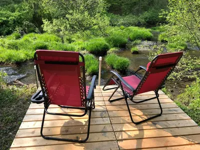 two chairs sitting on a wooden deck next to a stream at Red Creek Hideaway in Cooperstown NY in Cooperstown