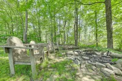 two wooden benches in a forest with trees and rocks at Cozy Woodland Home! Ski and Hike Coastal Connecticut in Killingworth