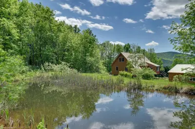 a barn and a pond with trees and mountains in the background at Catskills Cabin Rental with Hot Tub and Amazing Views! in Stamford