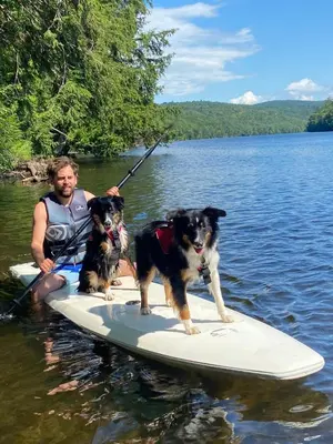 a man and two dogs on a paddle board in the water at Riverfront Ritz campsite in Lake Luzerne
