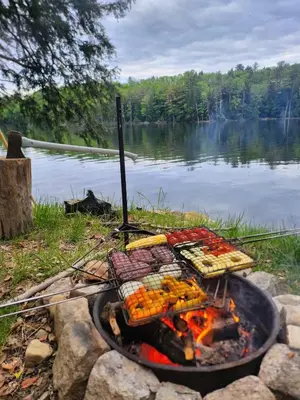 a grill with food on it next to a lake at Riverfront Ritz campsite in Lake Luzerne