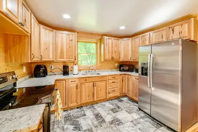 a kitchen with wooden cabinets and a stainless steel refrigerator at Creekside Cabin in Bainbridge with Wraparound Deck! in Sidney