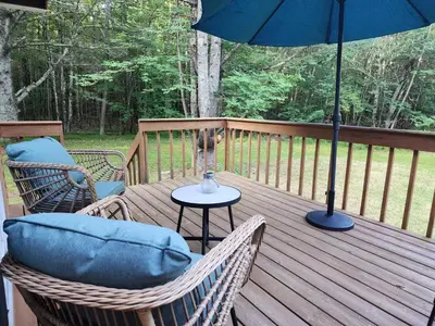 a wooden deck with chairs and an umbrella at Rustic Catskills Cabin with Hot Tub and Mountain Views in Prattsville