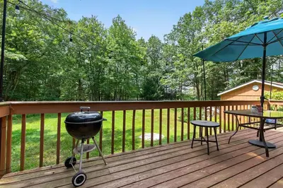a grill on a deck with a table and an umbrella at Rustic Catskills Cabin with Hot Tub and Mountain Views in Prattsville