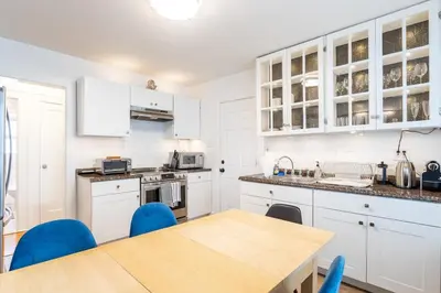 a kitchen with white cabinets and a wooden table at The B&W Haven 5BR Home with yard theater in Bridgeport