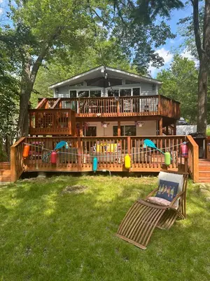 a large house with a deck and a chair in the yard at Majestic Lake Front Chalet in Tobyhanna