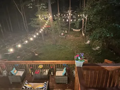 a deck with chairs and lights in the woods at night at Majestic Lake Front Chalet in Tobyhanna