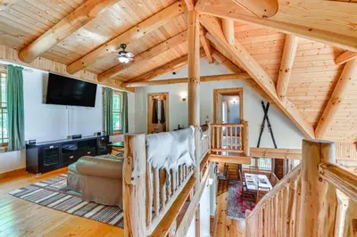 a living room with a staircase and a tv in a cabin at Lakefront Corinth Log Home Private Dock, Fire Pit in Lake Luzerne