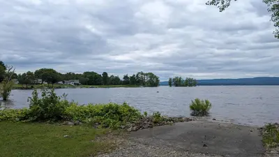 a large body of water with grass and trees at Adirondack Spirit in Gloversville