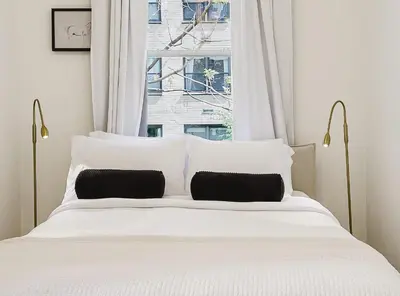 a white bed with two pillows in front of a window at Designer Home in Diplomat District in New York