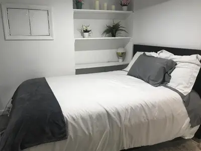 a bedroom with a bed with white sheets and gray pillows at 25-30 mins to Times Sq! in Corona