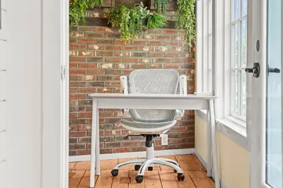 a white desk and a chair in front of a brick wall at Studio Flat Above Historic Cider Mill in Westport