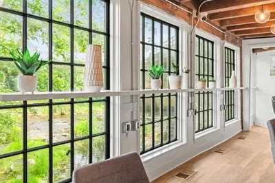 an open living room with large windows and plants at Studio Flat Above Historic Cider Mill in Westport