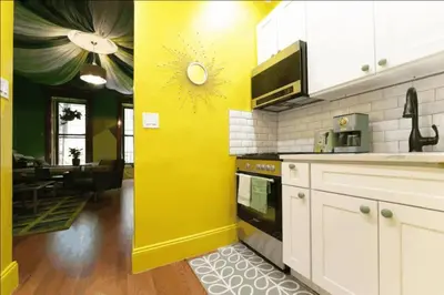 a kitchen with a yellow wall and a living room at The Green Room: 70s Groove Themed Studio in New York