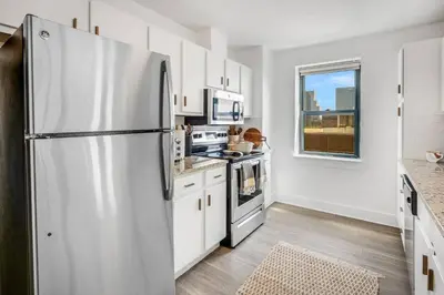 a kitchen with a stainless steel refrigerator and white cabinets at Penthouse Perfection with Unmatched Skyline Views in Stamford