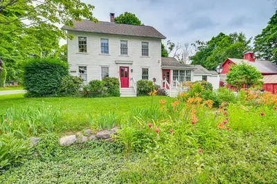 a white house with a red door and a garden at Historic Farmhouse Near Mountains and Colleges! in Westfield