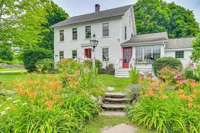 a white house with flowers in the yard at Historic Farmhouse Near Mountains and Colleges! in Westfield