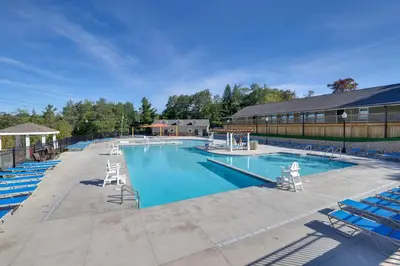 a large swimming pool with blue chairs and a building at Wooded Tobyhanna Home with Fire Pit and Lake Access! in Tobyhanna