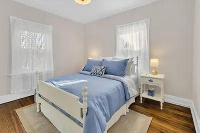 a white bedroom with a blue bed and two windows at Prime West Hartford Center- Timeless Charm in West Hartford