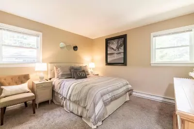 a bedroom with a bed and a chair and two windows at The Beautiful & Cozy Malvec Chalet in Tobyhanna