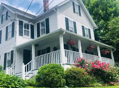 a white house with a porch with flowers on it at Stylish Victorian Beach House on pond in Rowayton