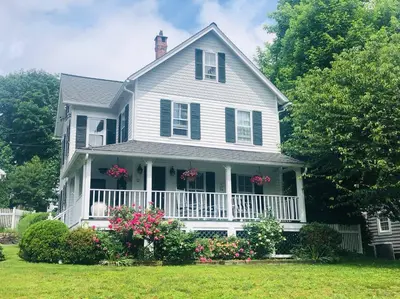 a white house with flowers in the front yard at Stylish Victorian Beach House on pond in Rowayton