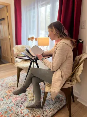 a woman sitting at a table with a book at Catskill Cabin Bird of Paradise 7 in Shandaken
