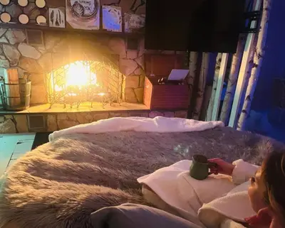 a woman laying in bed in front of a fireplace at Alpine Four Season Lodge, Belleayre NY, Sleeps 22, in Shandaken