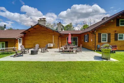 a log cabin with a patio and tables and chairs at Elegant Hudson Valley Retreat with Hot Tub and Pond in Austerlitz