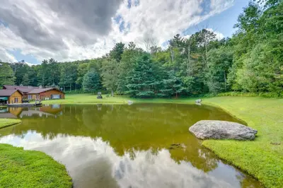 a pond in the middle of a yard with a house at Elegant Hudson Valley Retreat with Hot Tub and Pond in Austerlitz