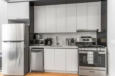 a kitchen with white cabinets and stainless steel appliances at Luxe Studio w Juliet Balcony in Upper East in New York