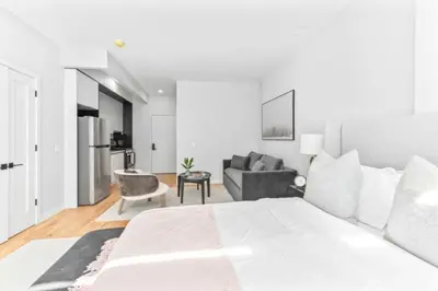 a white bedroom with a large bed and a couch at Luxe Studio w Juliet Balcony in Upper East in New York
