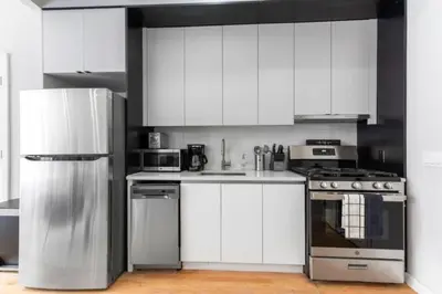 a kitchen with white cabinets and stainless steel appliances at Luxe Studio w Juliet Balcony in Upper East in New York