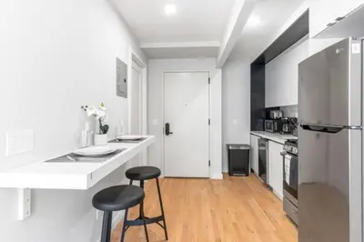 a white kitchen with a refrigerator and two stools at Luxe Studio with Charming Juliet Balcony in New York