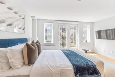 a white bedroom with a large bed and windows at Luxe Studio with Charming Juliet Balcony in New York