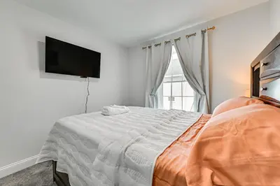 a white bedroom with a bed and a flat screen tv at 1 Mi to MGM Springfield Cozy Winter Duplex! in Springfield
