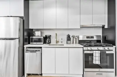 a white kitchen with white cabinets and appliances at Luxe Studio with Charming Juliet Balcony in New York